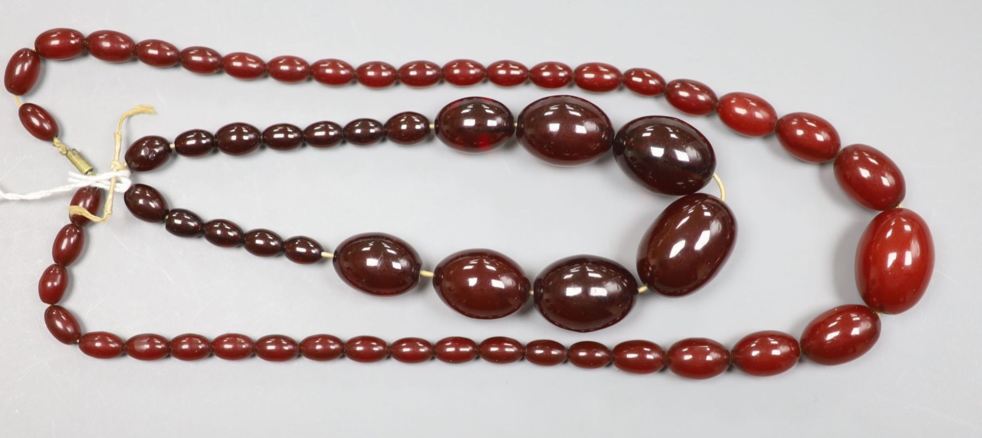 Two single strand graduated simulated cherry amber bead necklaces, 34cm & 58cm, gross 106 grams.